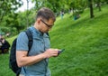Handsome man sitting on the grass outdoors and using smartphone