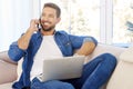 Young man using mobile phone and notebook while sitting on couch at home Royalty Free Stock Photo