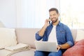Young man using mobile phone and notebook while sitting on couch at home Royalty Free Stock Photo