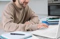 Young man using modern laptop for studying in kitchen, closeup. Distance learning Royalty Free Stock Photo