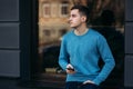 Young man is using the phone on the street. Handsome guy stand in front of window Royalty Free Stock Photo