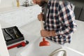 Young man using plunger to unclog sink drain in kitchen, closeup Royalty Free Stock Photo