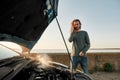 Young man using smartphone, calling for assistance while standing near his broken car with open hood Royalty Free Stock Photo