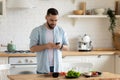 Young man using smartphone, cooking salad in kitchen, searching recipe