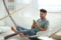 Young man using smartphone in hammock at home Royalty Free Stock Photo