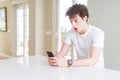 Young man using smartphone at home scared in shock with a surprise face, afraid and excited with fear expression