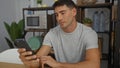 Young man using smartphone indoors at office with focused expression, showcasing modern technology and casual attire in a Royalty Free Stock Photo
