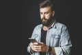 Young man using smartphone, listening music.Dark-haired bearded hipster with wireless earphones sliding screen of his mobile phone Royalty Free Stock Photo