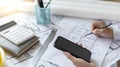 Young man using Smartphone plotting a system of building structures in blueprints Royalty Free Stock Photo