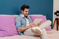 Young man using a tablet app to browse on internet sitting at home couch. Male teenager smiling and touching the screen Royalty Free Stock Photo