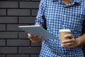 Young man using tablet computer holding coffee cup on street wall with copy space..Casual business man using modern internet Royalty Free Stock Photo