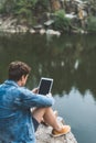 young man using tablet on nature while sitting on rocky