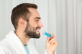 Young man using teeth whitening device on light background. Royalty Free Stock Photo