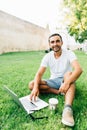 Young handsome man using and typing laptop computer in summer grass. Royalty Free Stock Photo