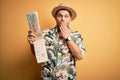 Young man on vacation wearing summer hat holding and looking at tourist map over yellow background cover mouth with hand shocked Royalty Free Stock Photo
