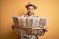 Young man on vacation wearing summer hat holding and looking at tourist map over yellow background scared in shock with a surprise Royalty Free Stock Photo