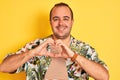 Young man on vacation wearing summer shirt striped t-shirt over isolated yellow background smiling in love showing heart symbol Royalty Free Stock Photo