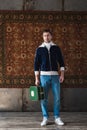 young man with vintage little suitcase in front of rug hanging