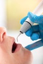 Young man visiting the dental office. Dentist hands in protective gloves using ultrasound to clean patient`s teeth Royalty Free Stock Photo