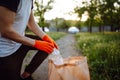 Young man volunteer picks up trash at the park. Plastic bottle is being collected by the man wearing orange gloves. Pollution,