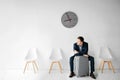 Young man wait for flight in room. He sit on chair and look to leaft. Guy lean on grey suitcase. Royalty Free Stock Photo