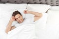 Young man waking up in bed with pillows