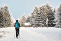 The young man is walking along the snow-covered hiking trail, there is a tourist shelter on the trail near the forest