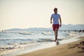 Young man walking on beach by water. Recreational walk on summer vacation. Holiday, health, active, lifestyle concept Royalty Free Stock Photo