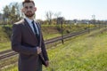 Portrait of a bearded guy of twenty-five years old, in a business suit, standing on an empty road in the afternoon. Against the Royalty Free Stock Photo