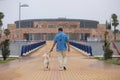 Young man walking with his brown Labrador retrieve dog. The photo is taken from behind. And in the background a building. Concept