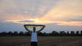 Young man walking with national blue-yellow banner on barley meadow at sunrise. Ukrainian guy going with raised flag of
