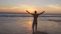 Young man walking at the ocean water on beach at sunset and raised hands. Sporty guy standing at sea shore and relaxing Royalty Free Stock Photo