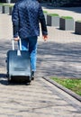 A young man walks along the cobbled sidewalk carrying a suitcase on wheels on a sunny day Royalty Free Stock Photo