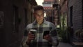 A young man walks along a narrow street late at night chatting on his smartphone and drinking coffee. A man in a warm Royalty Free Stock Photo