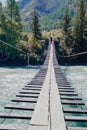 Young man walks along a suspension bridge across a mountain river Katun in the early autumn Royalty Free Stock Photo