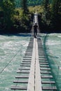 Young man walks along a suspension bridge across a mountain river Katun in the early autumn Royalty Free Stock Photo