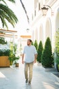 Young man walks down the street past a building with arches and tubed trees