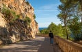 A young man walks on a mountain road traveling hitchhiking against the background of the sea