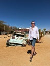 A young man walks near an abandoned old rusty car. Desert in Africa. Royalty Free Stock Photo