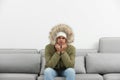 Young man in warm clothes freezing on sofa against background Royalty Free Stock Photo