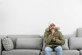 Young man in warm clothes freezing on sofa against background Royalty Free Stock Photo