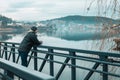 Young man in warm jacket standing on a bridge over the river in cold rainy day Royalty Free Stock Photo