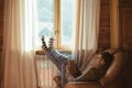 Young man in warm sweater reading by the window inside cozy log cabin