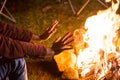 Young man warming up his hands over campfire