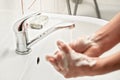 Young man washing hands under tap water with soap, focus on soapbar in background - importance of using lather for proper hygiene