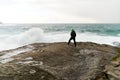 Young man standing on cliffs in front of the wild ocean with waves clashing against the rocks at Bunes Beach on Lofoten Islands in