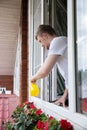 Young man watering blooming flowers looking out of window of country house Royalty Free Stock Photo