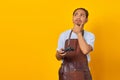 Young man wearing apron holding game controller looking aside with doubtful and skeptical expression on yellow background Royalty Free Stock Photo