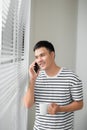 Young man wearing casual clothes talking on a mobile phone in the morning at a window with copy space Royalty Free Stock Photo