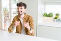 Young man wearing casual jacket sitting on white table pointing fingers to camera with happy and funny face Royalty Free Stock Photo